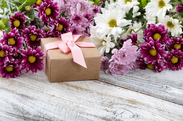 Gift box with mixed flowers in background on white weathered woo — Stock Photo, Image