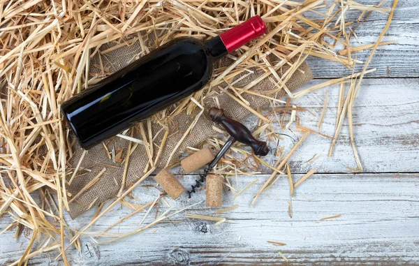 An unopen bottle of red wine plus corkscrew on top of straw and — Stock Photo, Image
