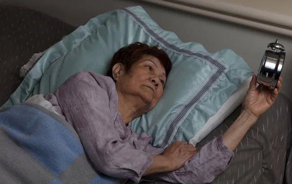 Restless senior woman glaring at alarm clock during nighttime wh — Stock Photo, Image