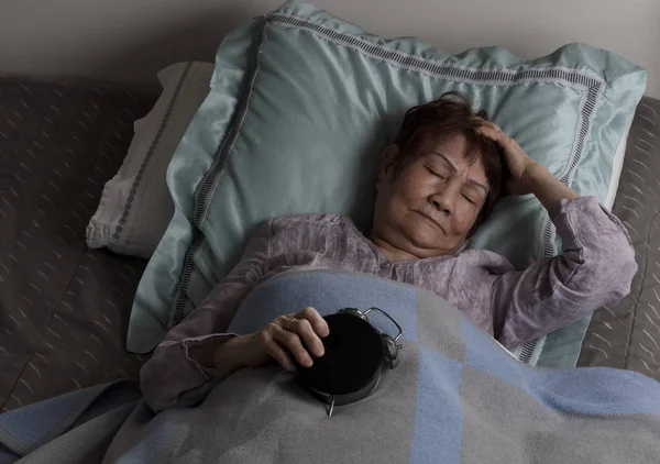 Mujer mayor inquieta sosteniendo el despertador boca abajo durante nig —  Fotos de Stock
