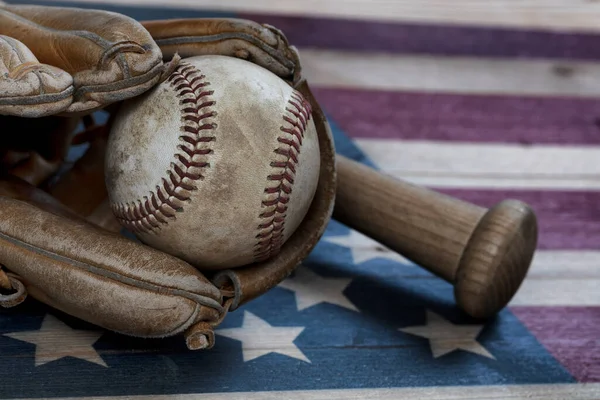 Closeup view of an old baseball, glove and traditional wood bat on rustic wooden United States Flag