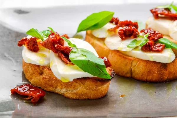 Sabrosos aperitivos italianos salados, o bruschetta, en rebanadas de baguette tostada adornada con albahaca —  Fotos de Stock