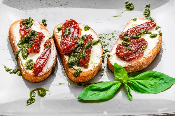 Délicieux apéritifs italiens salés, ou bruschetta, sur des tranches de baguette grillée garnie de basilic — Photo