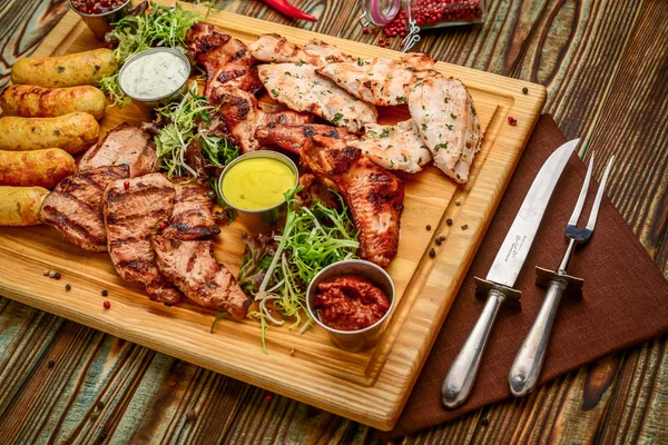 Assortiti deliziosi carne alla griglia e verdure con insalata fresca e salsa barbecue sul tagliere su sfondo di legno. Grande set di piatti di carne calda — Foto Stock