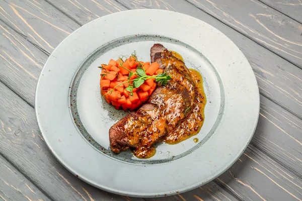 Grillat kött med sås och stuvade grönsaker på ett träbord — Stockfoto