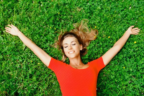 Jonge vrouw in rode jurk liggend op gras — Stockfoto