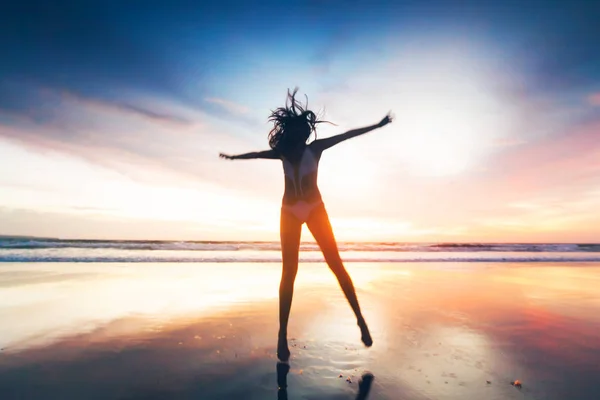 Mulher pulando na praia ao pôr do sol — Fotografia de Stock