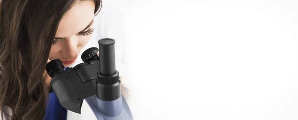 Médica olhando através de um microscópio — Fotografia de Stock