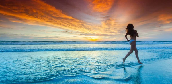 Žena běží na pláži při západu slunce — Stock fotografie