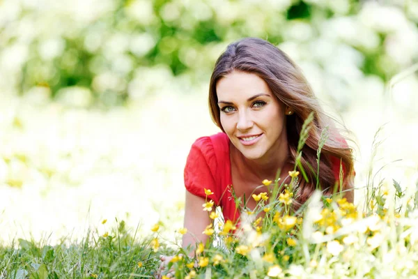 Jonge vrouw in rode jurk liggend op gras — Stockfoto