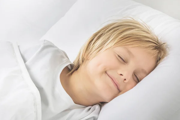 Улыбающийся мальчик спит в постели — стоковое фото