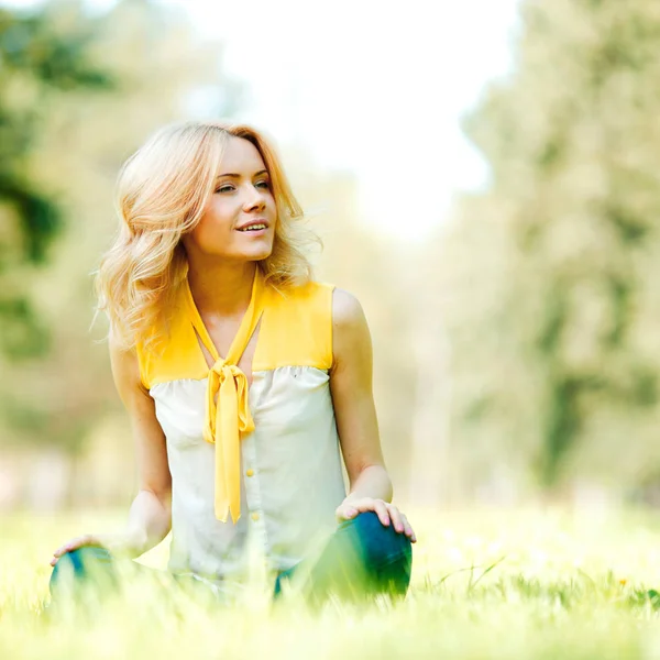 公園の芝生の上に座って美しい若いブロンドの女性 — ストック写真