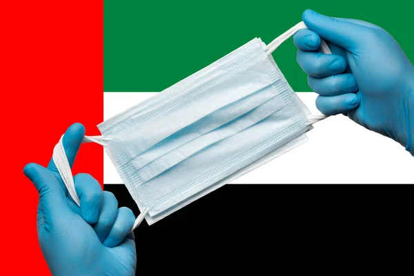 Medic holding respiratory face mask in hands in blue gloves on background national flag of United Arab Emirates UAE. Concept coronavirus quarantine