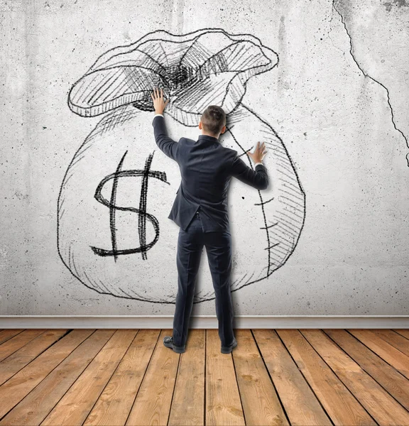 Zakenman raakt een schets van geld tas op betonnen muur. — Stockfoto