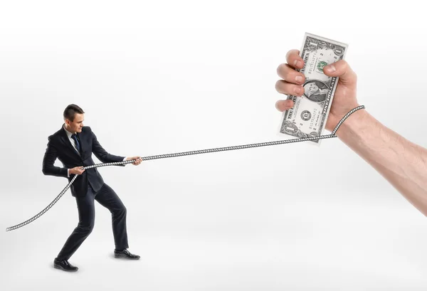 Businessman grabbed a big hand with cash dollars and pulls it by rope. — Stock Photo, Image