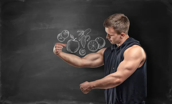 Fruit afgebeeld op zwarte achtergrond en fitness man zijn biceps onder de foto tonen — Stockfoto