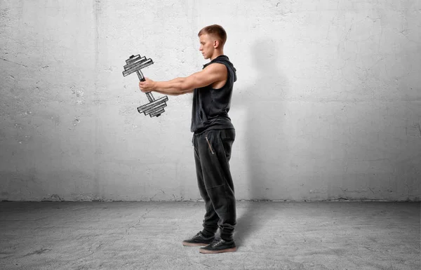Muscular sportsman full-height standing and holding a dumbbell, drawn on grey wall. — Stock Photo, Image