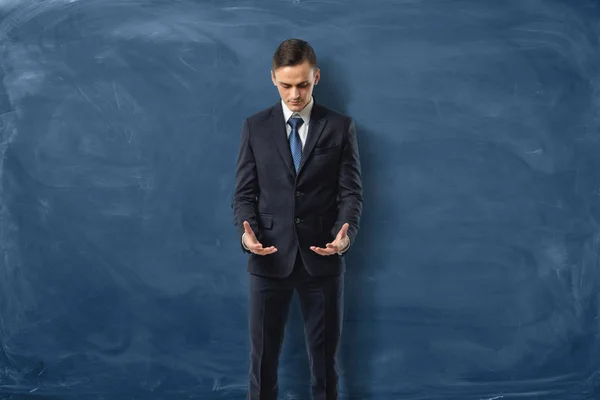 Hombre de negocios en traje de pie y mirando sus manos vacías sobre fondo azul oscuro . — Foto de Stock