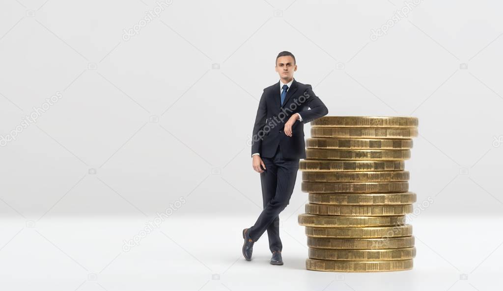Businessman leaning on stack of big golden coins