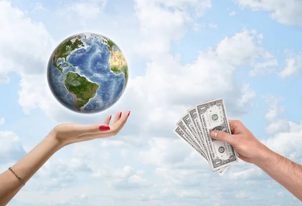 Mans hand giving dollar bills to female, which supports the planet Earth.