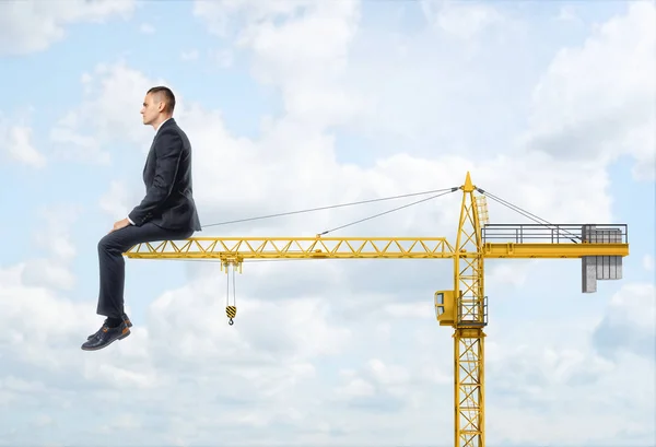 Huge businessman sitting on end of crane