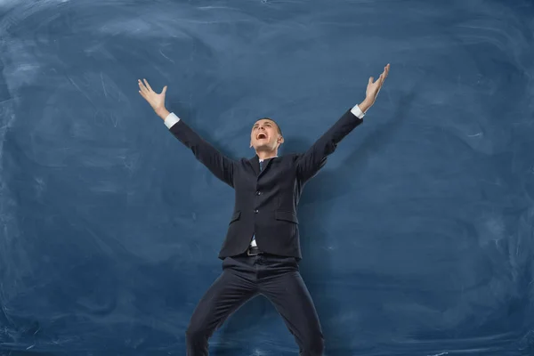 Businessman standing with splayed arms and shouting on the blue blackboard background. — Stock Photo, Image