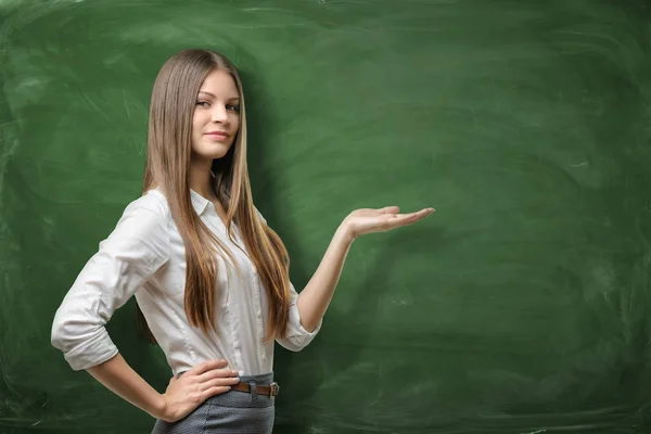 Mooie jonge zakenvrouw holding haar open palm en tonen op het lege gebied op groene schoolbord — Stockfoto