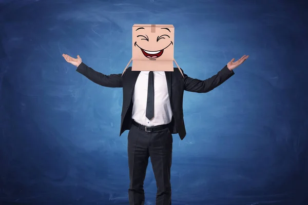 Бизнесмен поднимает руки вверх и носит коробку на голове с раскрашенным смеющимся лицом — стоковое фото