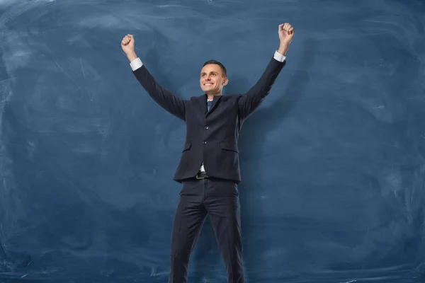Empresário com as mãos levantadas na vitória sobre fundo blackboard azul escuro — Fotografia de Stock