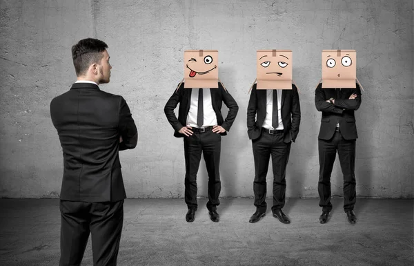 Empresário virou as costas e olhando para três homens usando caixas de papelão em suas cabeças . — Fotografia de Stock