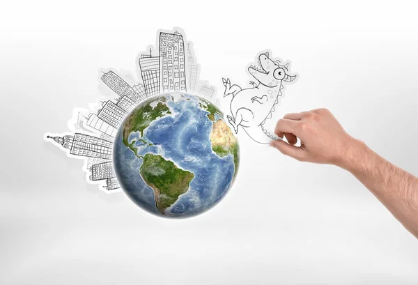 Mans hand holding cartoon funny monster going to attack city put around the globe on — Stock Photo, Image