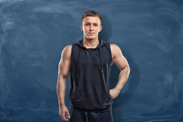 Musculoso joven en ropa deportiva está de pie sobre el fondo azul oscuro —  Fotos de Stock