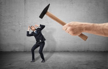 İşadamı tam yükseklikli umutsuz bir poz ve dev bir el ile bir çekiç threting onu gri arka plan üzerinde korkuttu