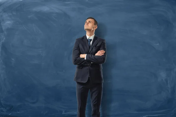 El hombre de negocios se mantiene con los brazos cruzados sobre el fondo azul de una pizarra — Foto de Stock