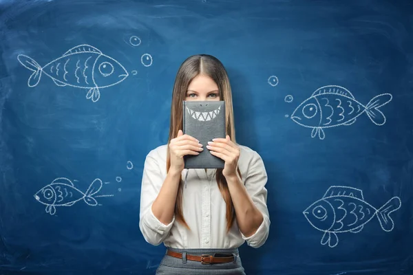 Vrouw houdt een laptop met getekende haaientanden op blauwe schoolbord achtergrond met getekende vis — Stockfoto