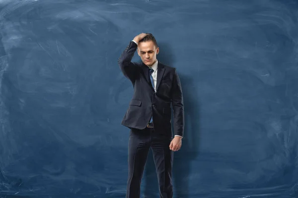 Empresário no fundo azul quadro segurando uma mão em sua cabeça em confusão . — Fotografia de Stock