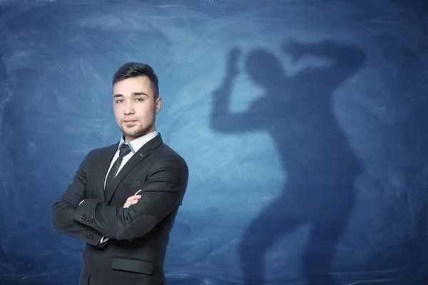 Geschäftsmann steht auf blauem Hintergrund mit einem Schatten, die Hände auf dem Kopf hinter sich — Stockfoto
