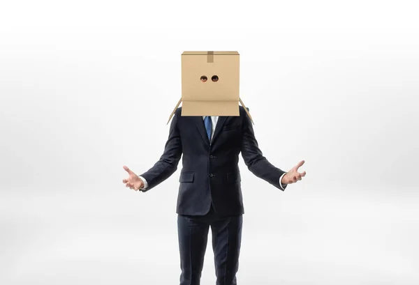 Empresário está ficando suas mãos para os lados com uma caixa na cabeça com buracos para os olhos no fundo branco — Fotografia de Stock