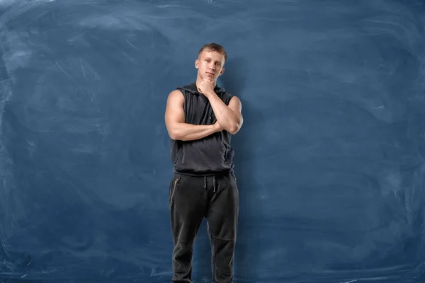 М'язистий молодий чоловік стоїть і думає тримати голову рукою на синьому крейдяному фоні — стокове фото