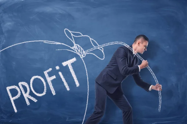 Бизнесмен тянет большой мешок с деньгами на веревке на синем фоне — стоковое фото