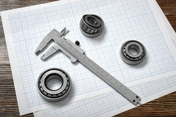 A large vernier scale lying on cross section paper with three bearings around it on wooden background.