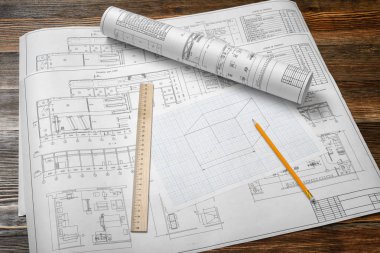 Bir dizi açın ve bir kalem ve yanında yatan bir cetvel ile ahşap masa arka plan üzerinde planları kadar haddelenmiş.