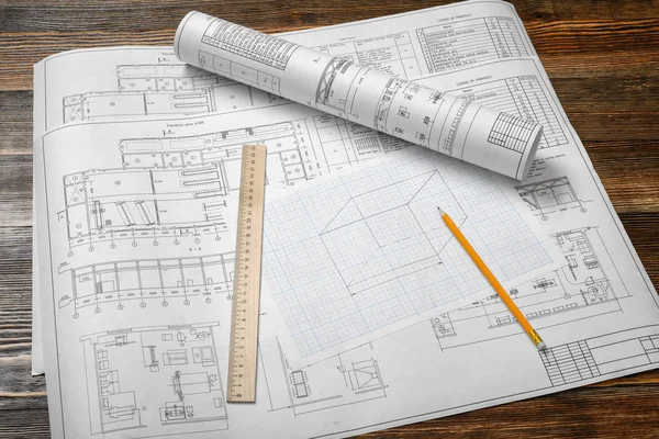 Un ensemble de plans ouverts et enroulés sur fond de table en bois avec un crayon et une règle couchée à côté . — Photo