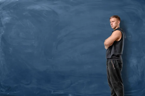 Musclé jeune homme est debout ses bras croisés et regardant vers l'avant sur fond de tableau bleu — Photo