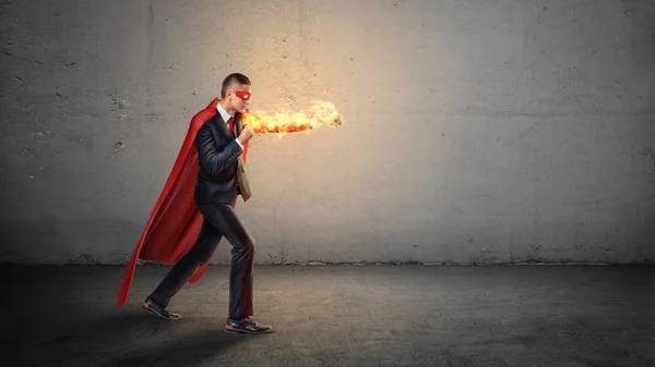Een zakenman in een rode superheld cape en een vlammende hand gooien stoten op een onzichtbare vijand op concrete achtergrond. — Stockfoto