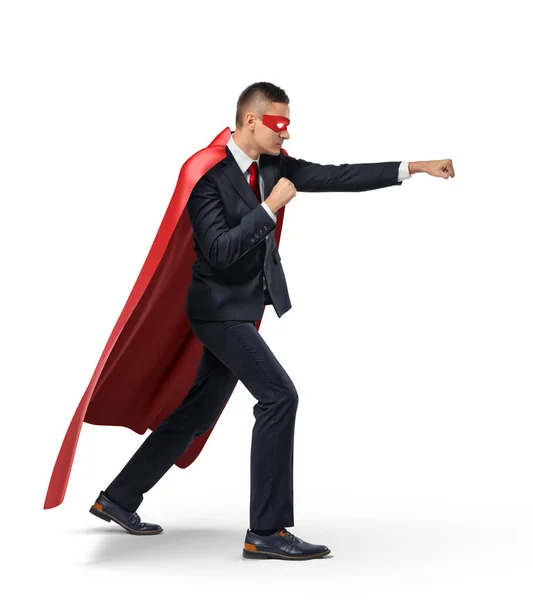 Un homme d'affaires dans une cape rouge de super-héros et un masque debout en vue latérale en position de poinçon sur fond blanc . — Photo