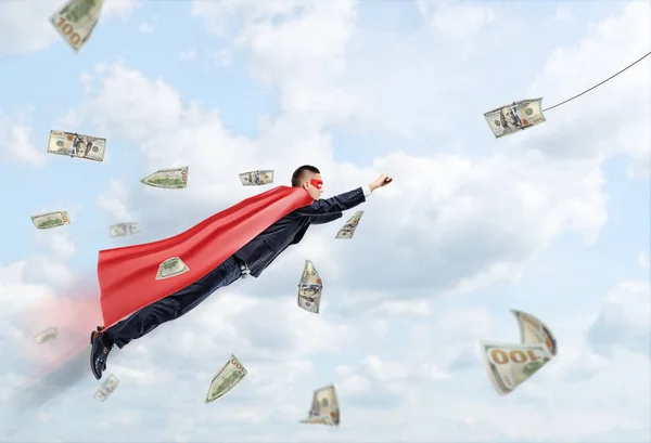 Een zakenman die het dragen van een rode superheld Kaap vliegen door de wolken na een dollarbiljet. — Stockfoto