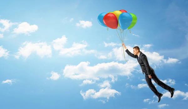 Een zakenman die houden van een partij van kleurrijke ballonnen die hem laten vliegen door de wolken. — Stockfoto