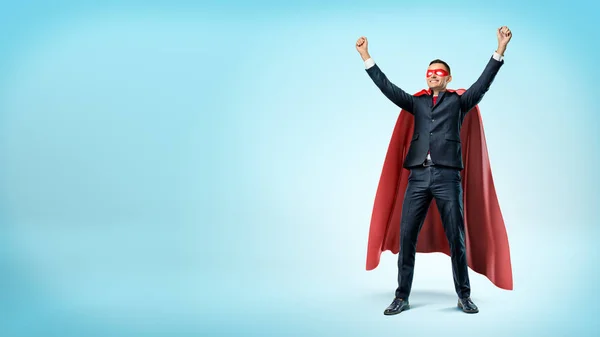 En glad affärsman i en superhjälte röd cape står i seger pose på blå bakgrund. — Stockfoto