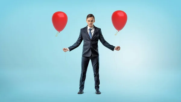 Een zakenman die permanent op blauwe achtergrond met een rode ballon in elke hand. — Stockfoto
